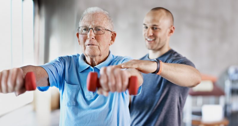 An instructor coaching an older man through a strength exercise