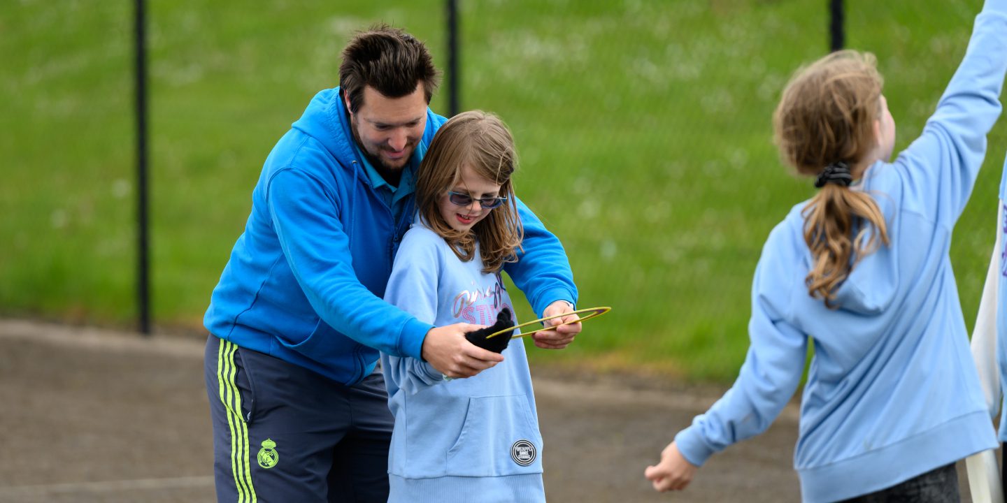 A coach helping a girl throw a frisbee